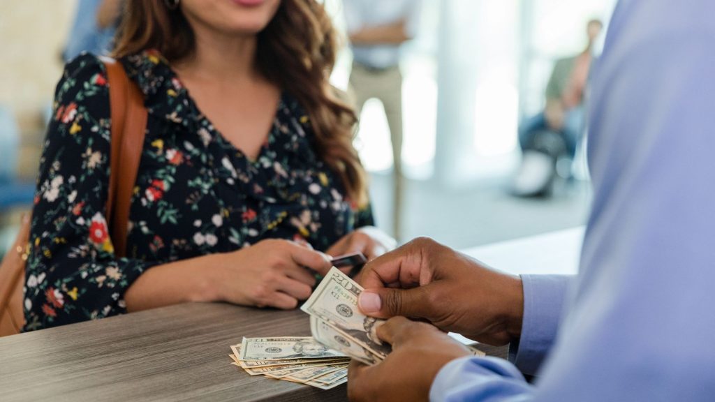 Woman paying with cash at a business counter - Associated Currency Exchanges