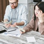 A man and woman hold money while a bill sits on the table.
