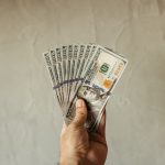 Someone holding several 100 dollar bills in their hand.