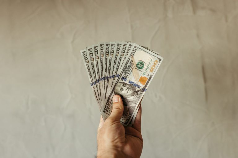Someone holding several 100 dollar bills in their hand.