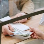 A man giving cash to a bank teller.