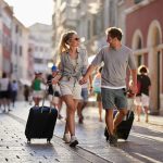 A couple holding hands while pulling their luggage.